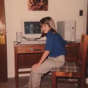 Photo of me as a kid, early 2000s. I'm sitting at my desk. I'm proudly showing off my computer, which is now extremely dated. The CRT monitor looks almost as big as me.